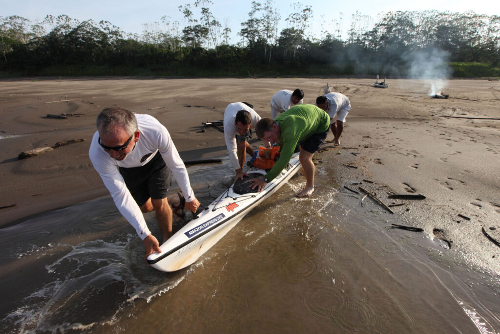 Amazon Express expedition team members from left, Jeff Wueste, Ian Rolls and West Hansen and local guides push their kayak out of their campsite on Isla de Loreto on the Colombian side of the Amazon River. This was the team's final push through Peru to the Brazilian border. Amazon Express expedition October 27, 2012. Photo by Erich Schlegel